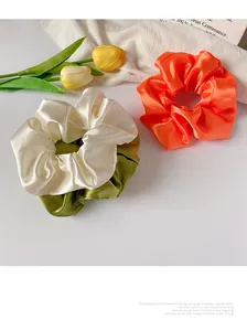 Détail de chouchous en satin orange, crème et vert olive avec texture soyeuse élégante