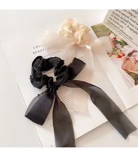 Detailed view of organza bow scrunchies in cream and black on a magazine backdrop
