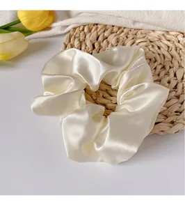 Détail de la texture d'un chouchou en satin blanc crème avec plis sur un tapis de paille
