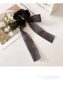 Detail view of a black organza bow scrunchie with long ribbons on a white surface