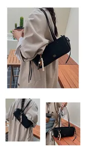 Detail of minimalist black baguette bag with beaded charm and gold text branding