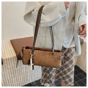 Detail of a brown suede shoulder bag with a beaded bohemian charm and metal logo