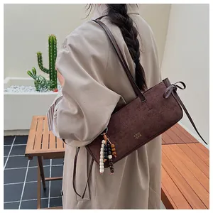 Detail of dark brown suede shoulder bag with bow decor and beaded tassel charm