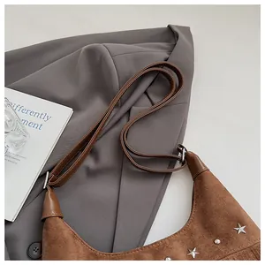 Détail d'un sac seau en daim marron avec rivets étoiles argentées et sangle en cuir