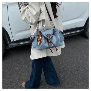 Détail du sac seau en denim bleu avec garniture en cuir et breloque en perles de bois