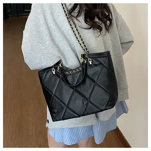 Détail d'un sac cabas noir matelassé avec chaîne dorée porté par un mannequin en style décontracté