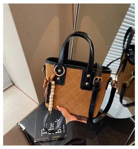 Detailed view of brown suede bucket bag featuring white diamond stitching and wood beads