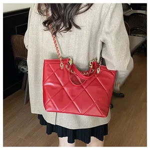 Détail d'un sac cabas rouge matelassé avec chaîne dorée porté par un mannequin en café