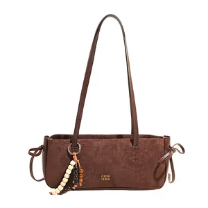 Brown suede underarm bag with wooden bead charm and minimalist brand logo