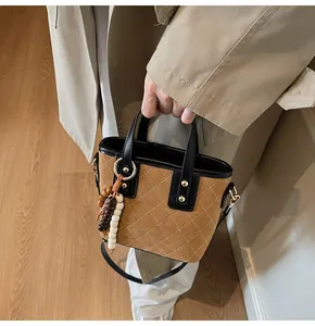 Close-up of quilted camel suede bucket bag with black leather handle and beaded charm