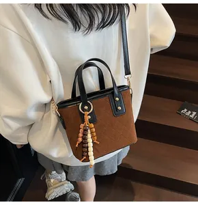 Detailed macro of brown suede bucket bag featuring diamond stitching and wood bead charm