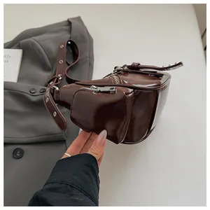 Detail of glossy brown leather shoulder bag with silver rivets and metallic zippers