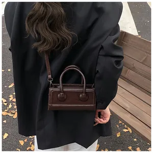 Detail of a dark brown mini leather crossbody bag worn over a black blazer in autumn
