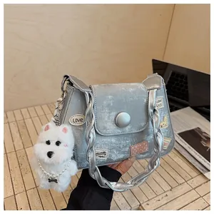 Bolso bandolera plateado con parches de gato y colgante de perro sobre mesa madera