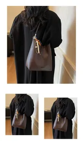 Détail du sac seau rétro marron avec décoration de pompon et perles en bois sur la sangle