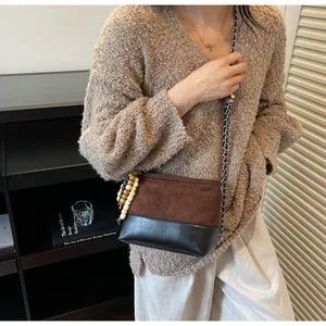 Détail du sac seau matelassé bicolore avec bandoulière chaîne et pendentif en perles bois