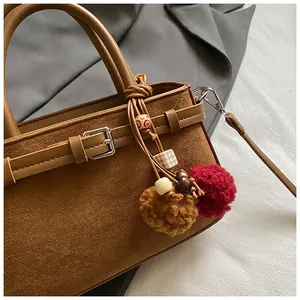 Detailed macro shot of brown suede handbag featuring colorful fuzzy ball bag charms