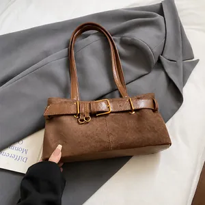Détail d'un sac bandoulière en daim marron foncé avec boucle dorée sur un blazer gris