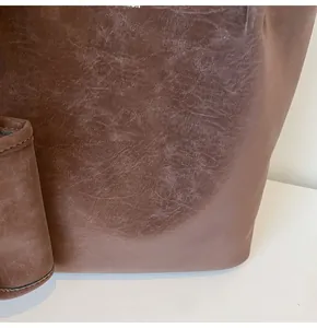 Macro detail of the dark brown oil-wax leather texture and neat stitching on the tote bag