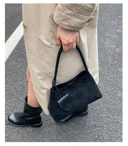 Detailed view of a black suede handbag featuring a knotted strap and circular charm