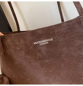 Detail of dark brown tote bag showing matte leather texture and white logo lettering