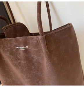 Close-up of the vintage leather texture and white printed logo on a large brown tote bag