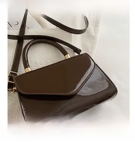 Détail d'un sac bandoulière en cuir verni marron foncé avec finitions dorées chic