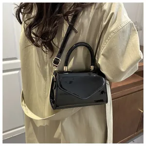 Détail d'un sac bandoulière chic en cuir verni noir porté avec un trench-coat beige classique