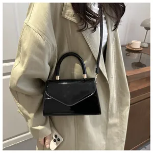Détail du mini sac en cuir verni noir brillant avec finitions dorées sur un manteau beige
