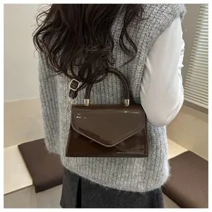 Gros plan d'un sac bandoulière en cuir verni marron foncé montrant la texture et les dorures