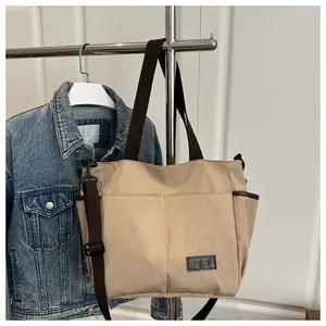 Détail d'un sac cabas en toile beige avec deux poches avant et une étiquette en cuir marron