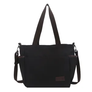 Sac cabas minimaliste en toile noire avec anses brunes et bandoulière réglable sur blanc