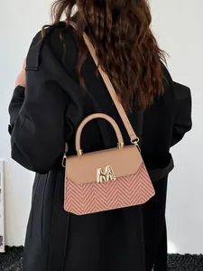 Chic beige and pink chevron crossbody bag with gold M buckle worn on a black coat