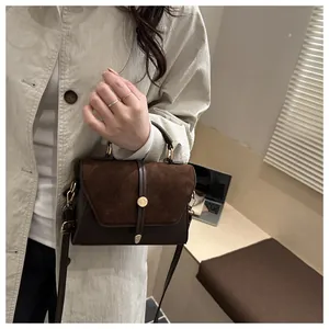 Detail of dark brown vintage crossbody bag with metal buckle shown on a beige trench coat