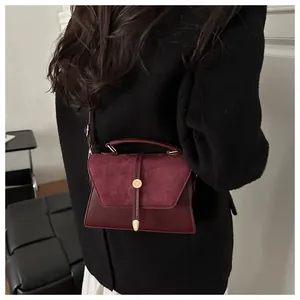 Detail of burgundy crossbody bag featuring suede texture contrast and gold metal clasp