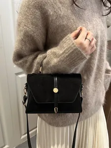 Elegant black crossbody bag with gold metal buckle shown in a stylish indoor setting