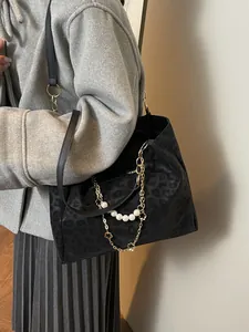 Black leopard print tote bag with gold chain and pearl strap detail on a stylish model