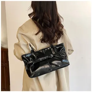 Détail d'un sac sous les bras noir brillant avec design plissé et boucle argentée