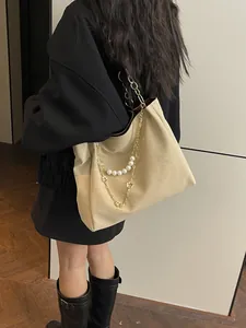 Beige tote bag with gold and pearl chains shown on shoulder in a stylish indoor setting