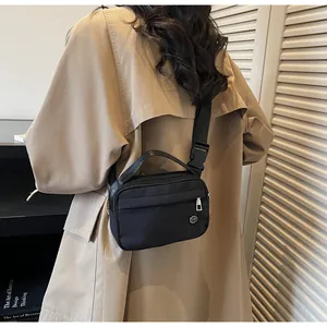 Détail de la bandoulière réglable du sac en nylon noir porté sur un trench-coat kaki