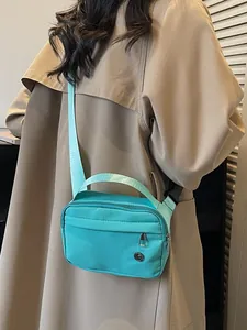 Petit sac bandoulière en nylon bleu clair porté par un mannequin en trench kaki