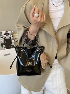 Borsa a secchiello nera lucida con catena argento e ciondolo a orsetto su modella