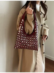 Detail of burgundy hobo bag featuring silver metal rivets and glossy finish on the shoulder