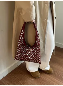 Detail view of burgundy leather shoulder bag with silver rivets carried by a model