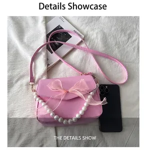 Rosafarbene Handtasche aus Leder mit Netzbogen und Perlenhenkel neben einem Handy
