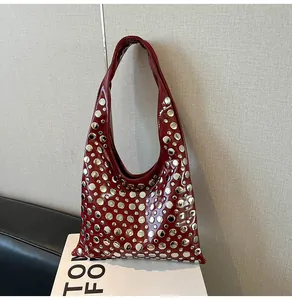Detail of dark red patent leather shoulder bag with silver round metal rivets and wide strap