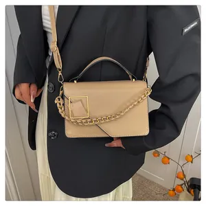 Détail d'un sac bandoulière beige avec boucle dorée et chaîne porté par un modèle