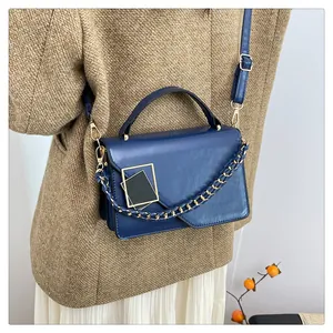 Détail d'un sac à main bleu marine avec chaîne dorée et bandoulière porté par un mannequin