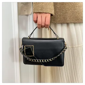 Détail d'un sac à main noir en cuir avec fermoir carré doré et grosse chaîne métallique