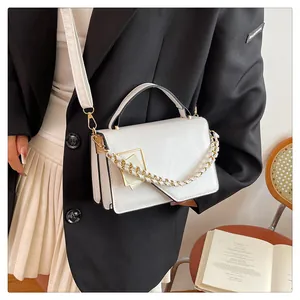 Détail d'un sac à main blanc avec boucle dorée et bandoulière en chaîne tressée